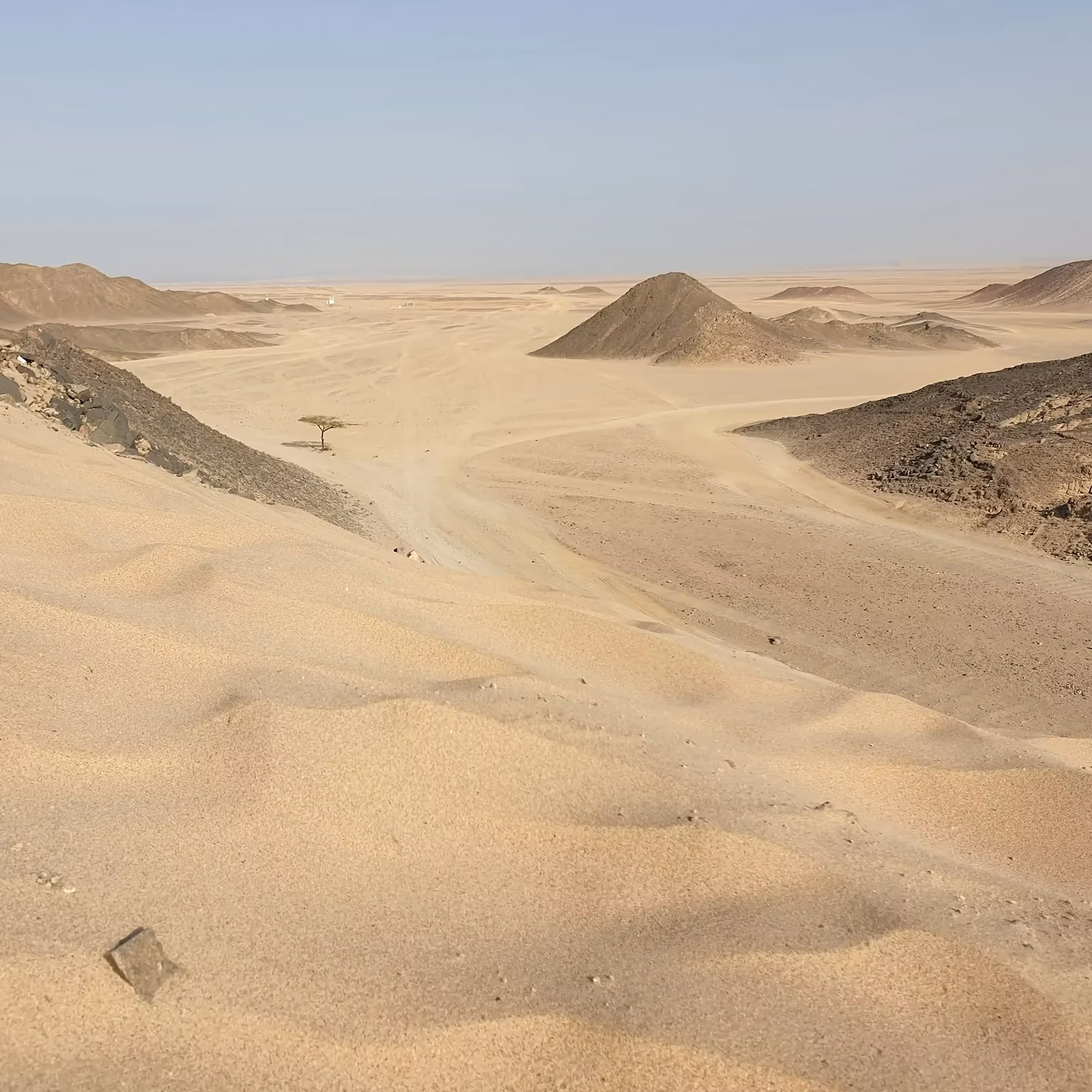 Een brede zandvlakte met duinen en rotsachtige heuvels onder een heldere lucht