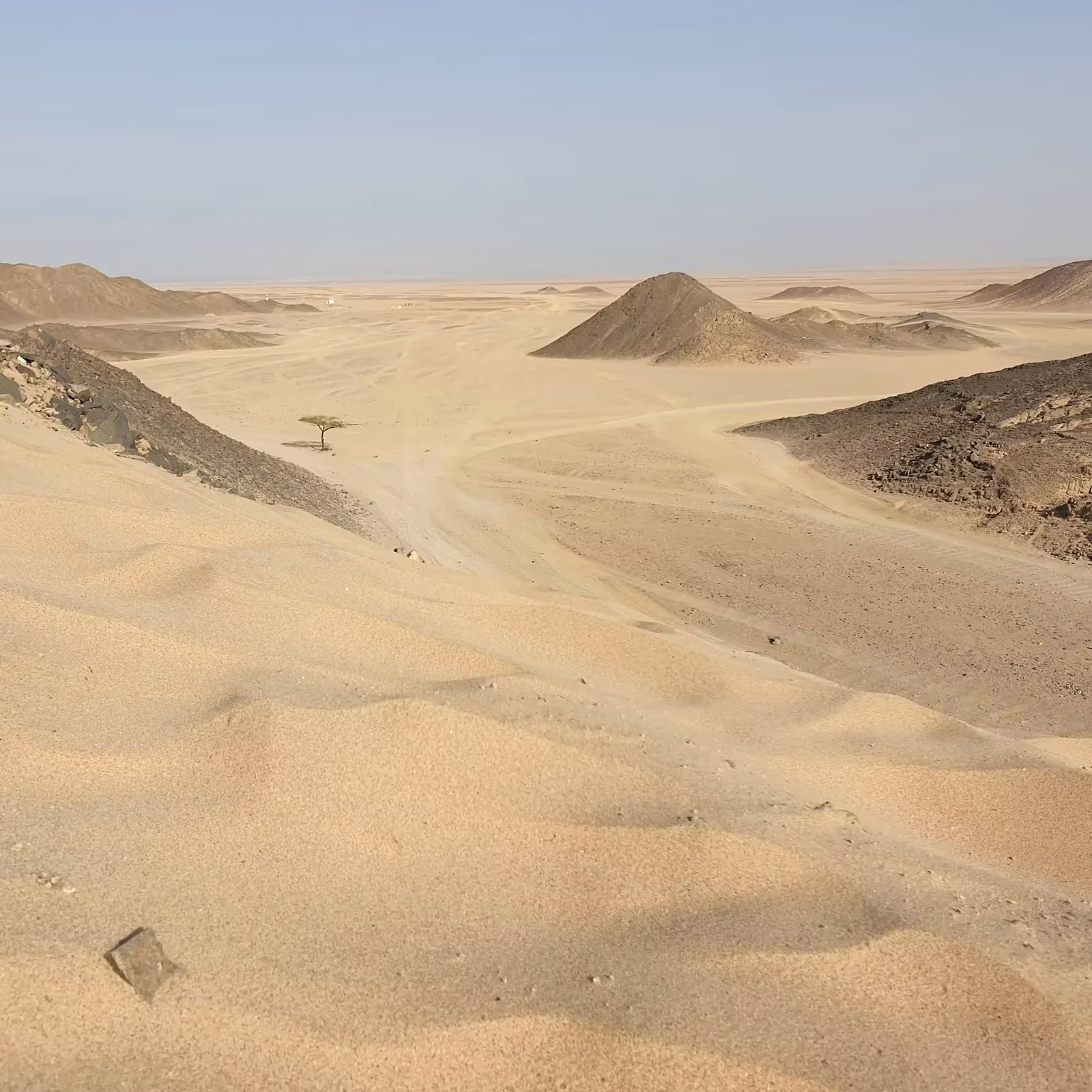 Een brede zandvlakte met duinen en rotsachtige heuvels onder een heldere lucht