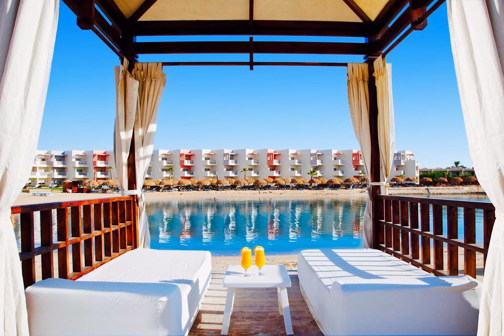 Cabana met twee ligbedden en gordijnen, uitzicht over de lagune op de kamers, SUNRISE Crystal Bay Resort in Hurghada