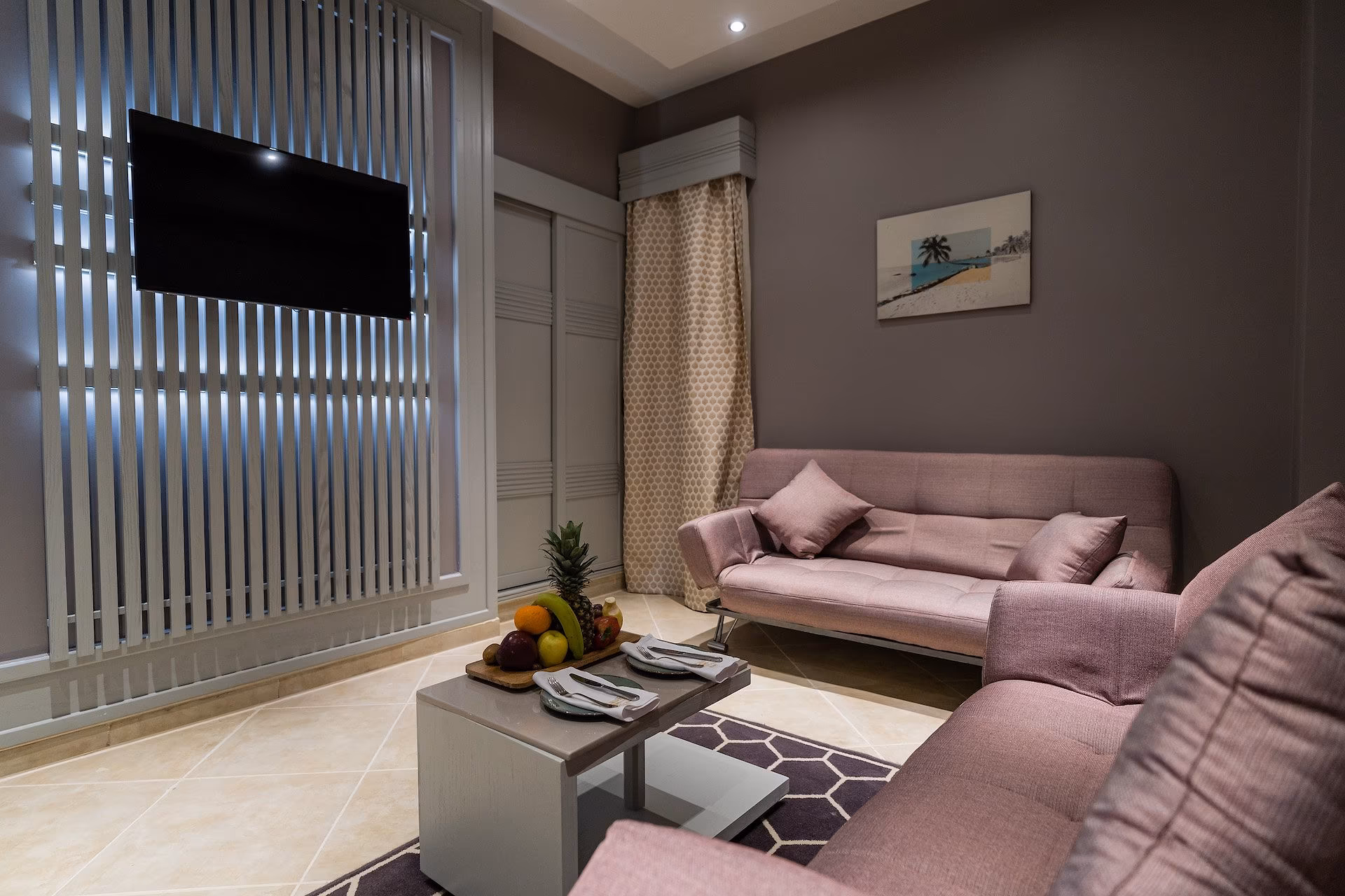 Woonkamer van de Family Suite met roze bank en slaapbank, tv en lamellenwand, SUNRISE Crystal Bay Resort in Hurghada