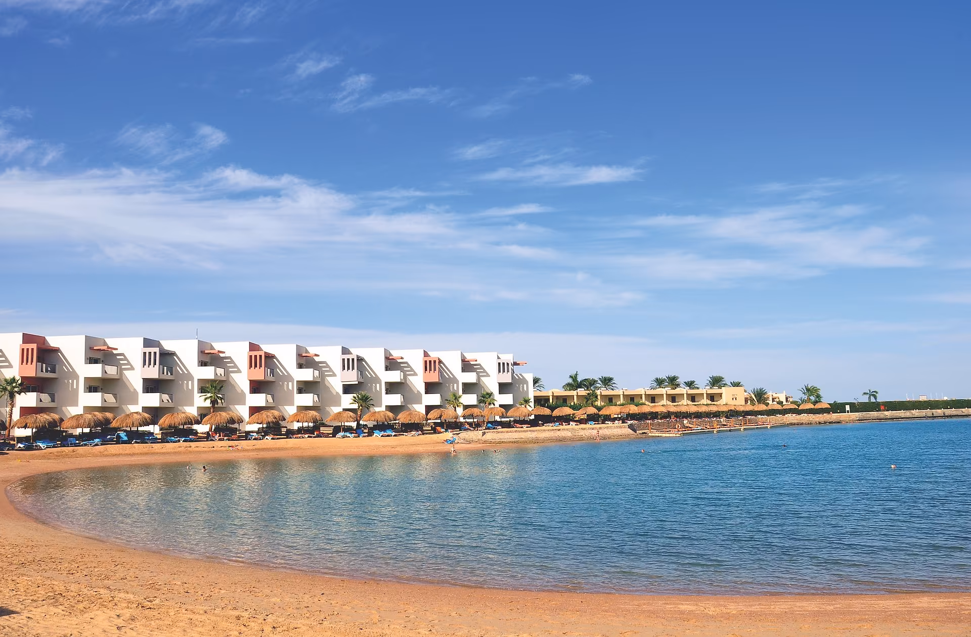 Zandstrand aan de lagune met strandparasols en de kamers erachter, SUNRISE Crystal Bay Resort in Hurghada