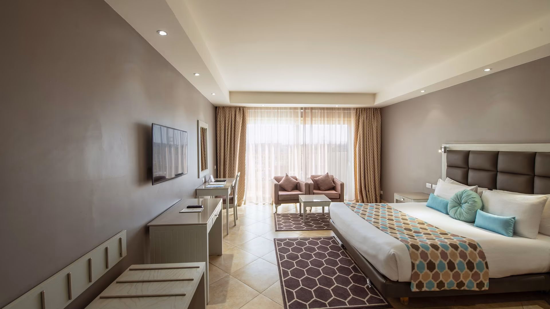 Lange kamer met kingsize bed, tv aan de wand en twee fauteuils bij het balkon, SUNRISE Crystal Bay Resort in Hurghada